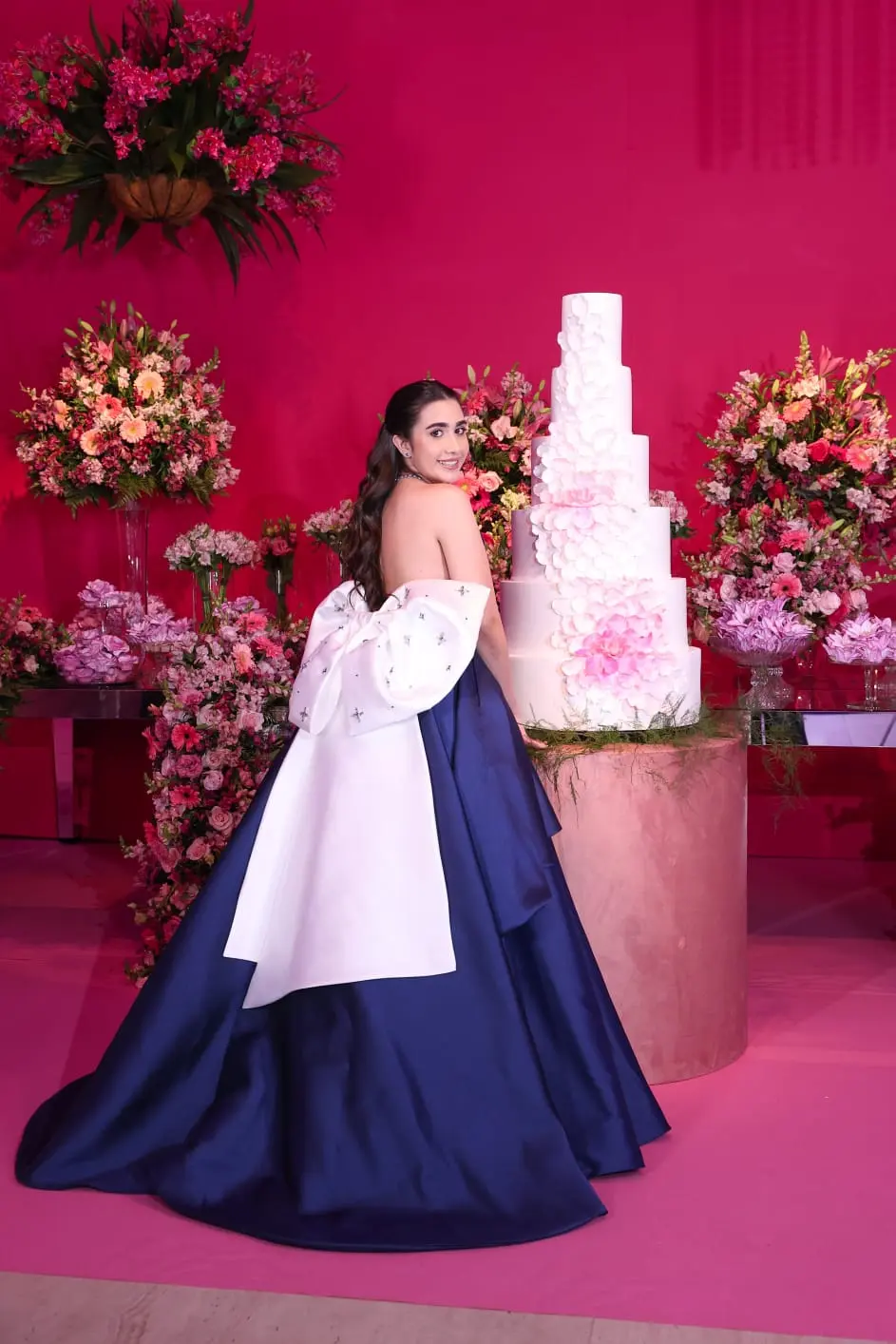 Jovem diante do bolo e da decoração de sua festa de 15 anos